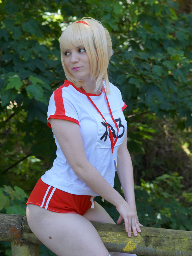 A person in a sporty outfit poses playfully while seated on a wooden railing, surrounded by lush green foliage.