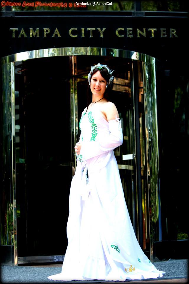 A woman in a white gown with green embellishments stands in front of a modern building with 'Tampa City Center' prominently displayed.