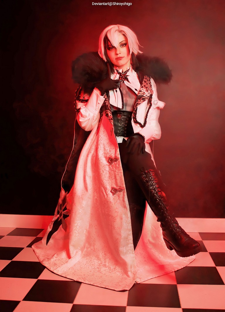 A person dressed in elaborate costume with a long, flowing cloak and black boots, posing in front of a red background with a checkered floor.