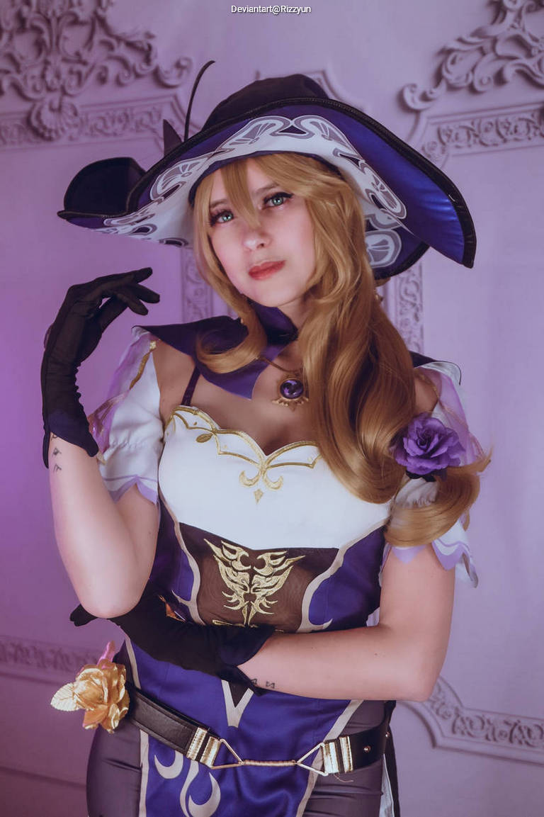 Cosplayer wearing an elegant purple and white dress with gold accents, a large ornate hat, and gloves, posing with a serene expression.