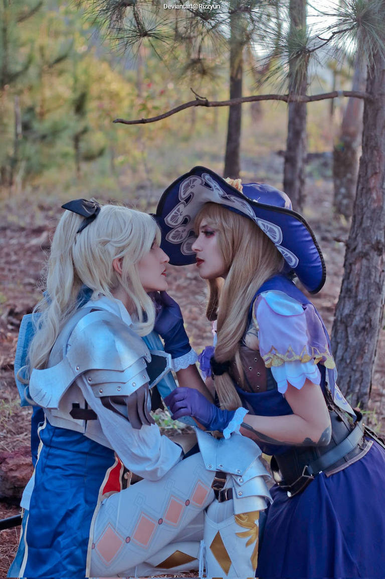 Two cosplayers in a forested setting, one wearing a blue outfit with armor and the other in a purple dress and hat, leaning in closely as if sharing a moment.