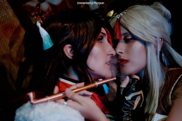 Close-up of two women cosplaying as characters, sharing an intimate moment. One holds a flute, adorned with traditional clothing and accessories.