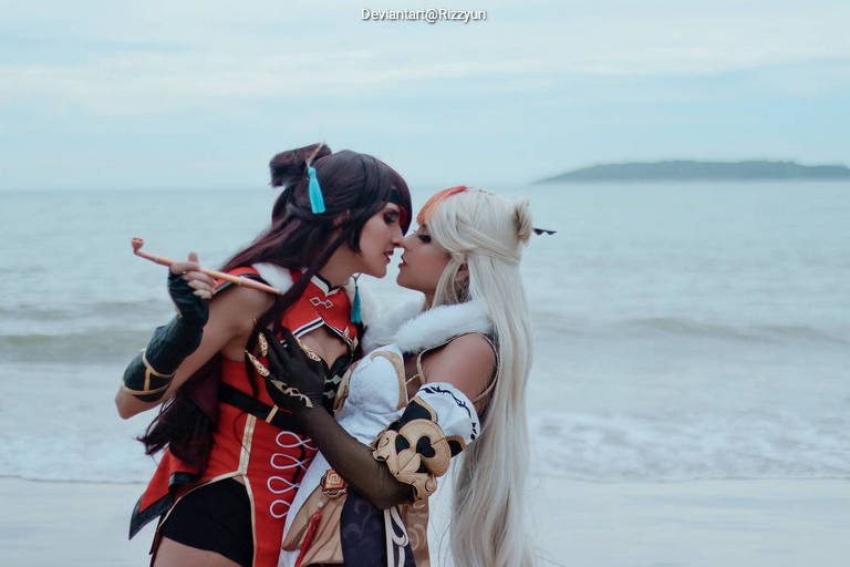 Two cosplayers in a romantic pose on a beach, wearing elaborate costumes, with ocean waves in the background.