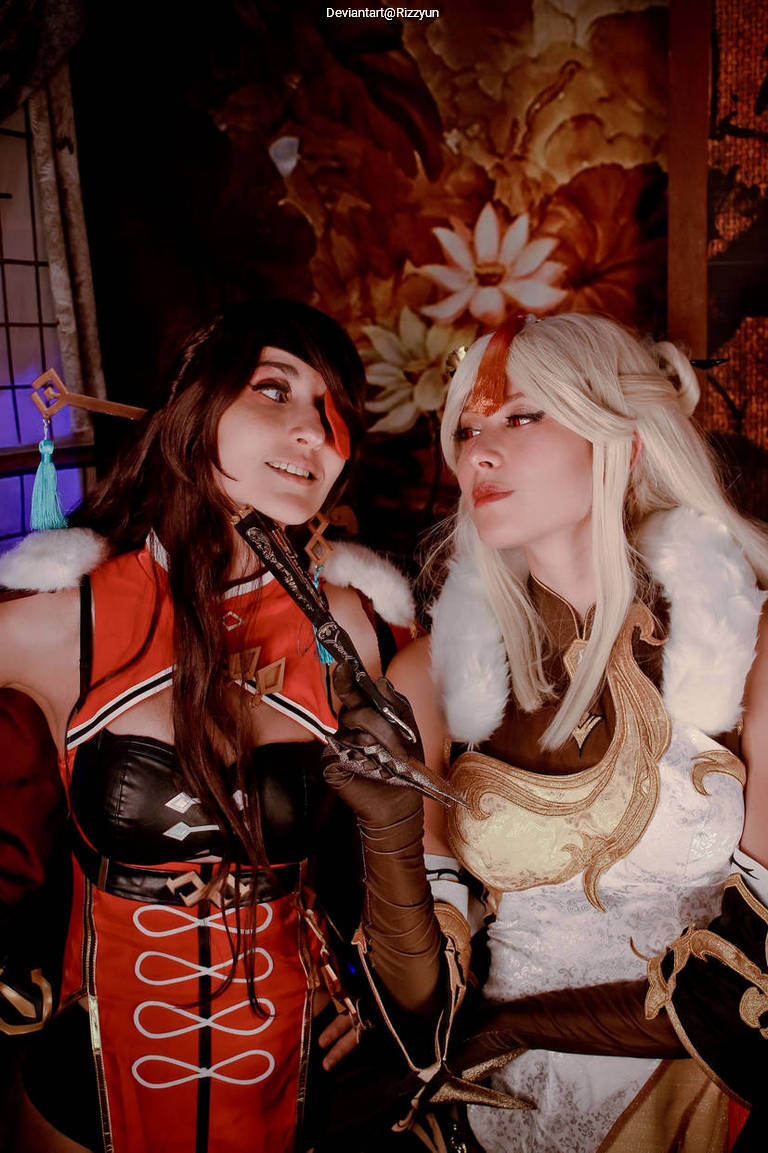 Two women in elaborate costumes interacting in a vibrant setting, with ornate background featuring flowers.