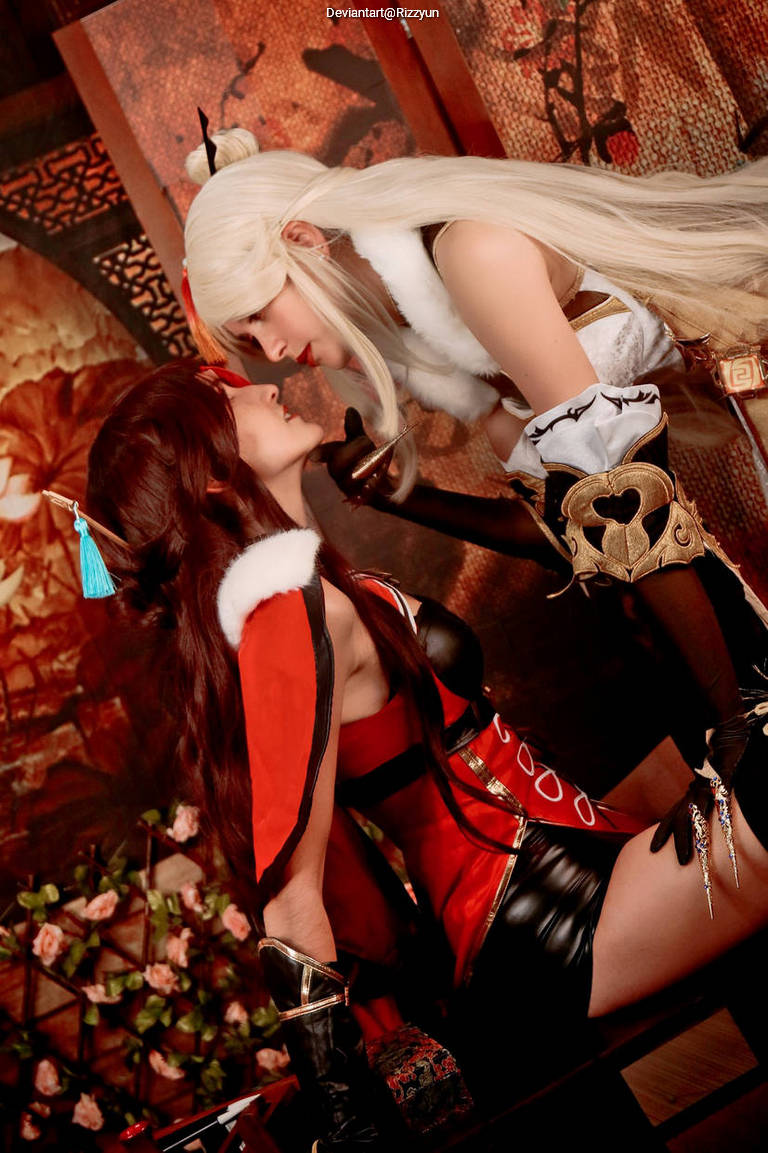 Two characters in elaborate costumes are posed closely together in a romantic setting. The character on the left has long dark hair and a red outfit with a white fur collar, while the character on the right has long white hair and a detailed outfit featuring gold accents.