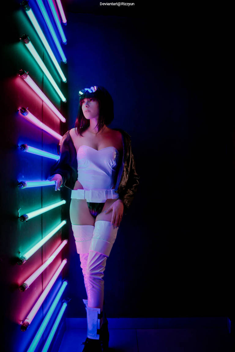A person posing next to colorful neon lights, wearing a stylish outfit with distinct lighting effects.