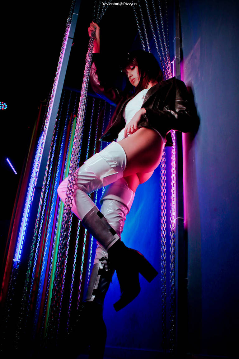A model poses against a colorful backdrop with chains, wearing a black jacket and thigh-high white boots, accentuated by neon lighting.