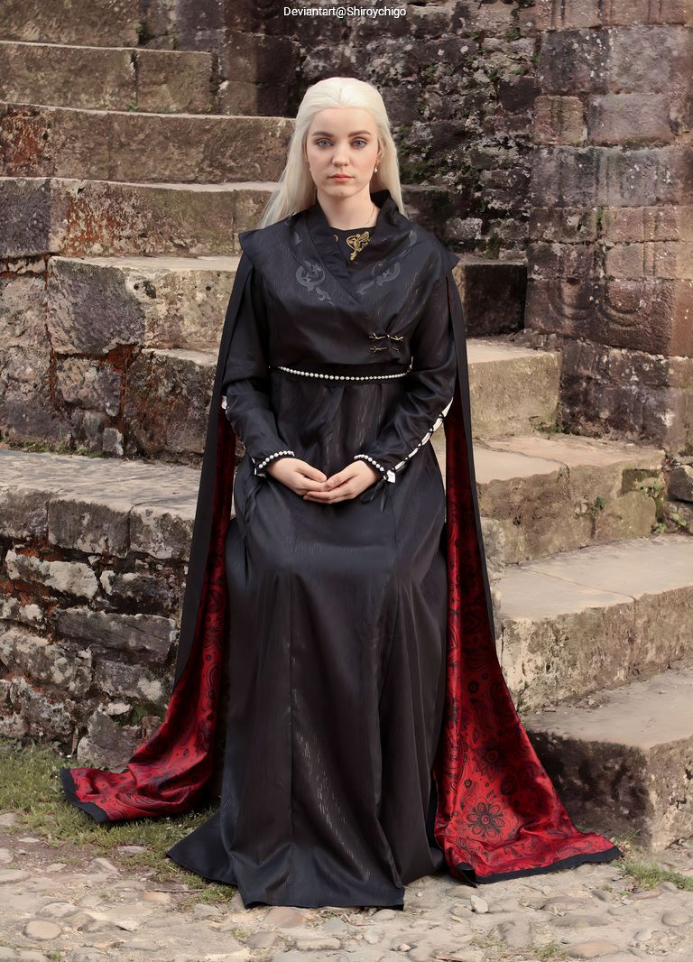 A person dressed in an elegant dark gown with a red and black cape, sitting on stone steps, looking directly at the camera.