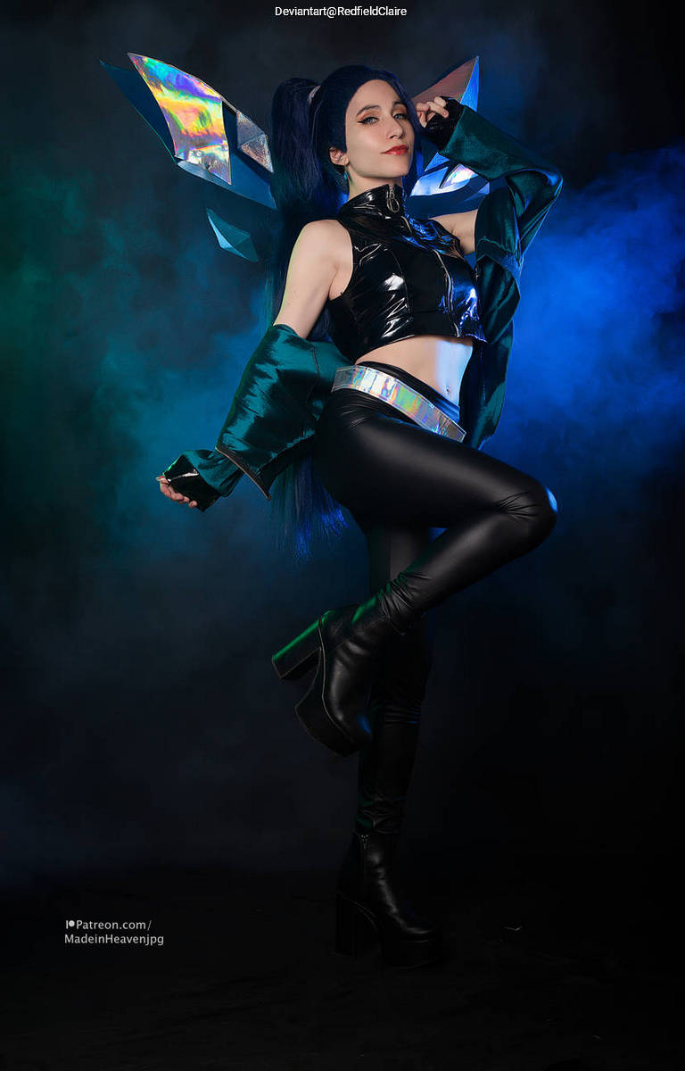 A person in a futuristic outfit with metallic elements and dramatic hair posing confidently against a colorful smoke backdrop.