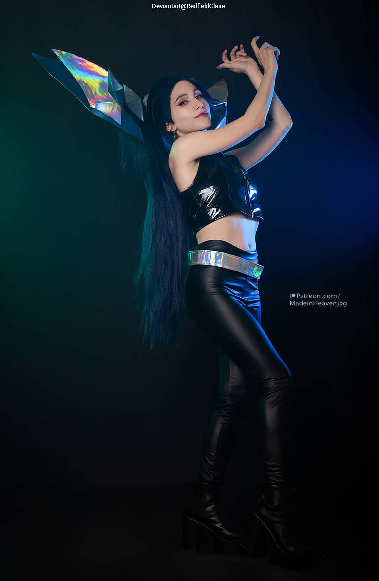 A person in a futuristic costume featuring metallic and holographic elements, with long dark hair, posed dramatically against a dark background with colorful lighting.