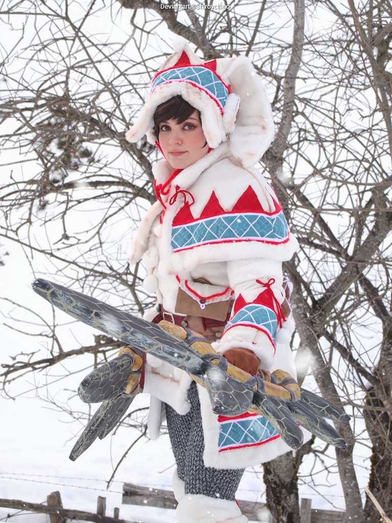A person dressed in a vibrant, winter-themed costume with colorful patterns stands in a snowy landscape, holding a large, ornate weapon.