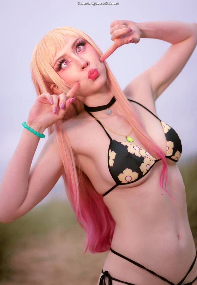A person in a black and floral bikini making playful expressions with pink hair and long eyelashes.