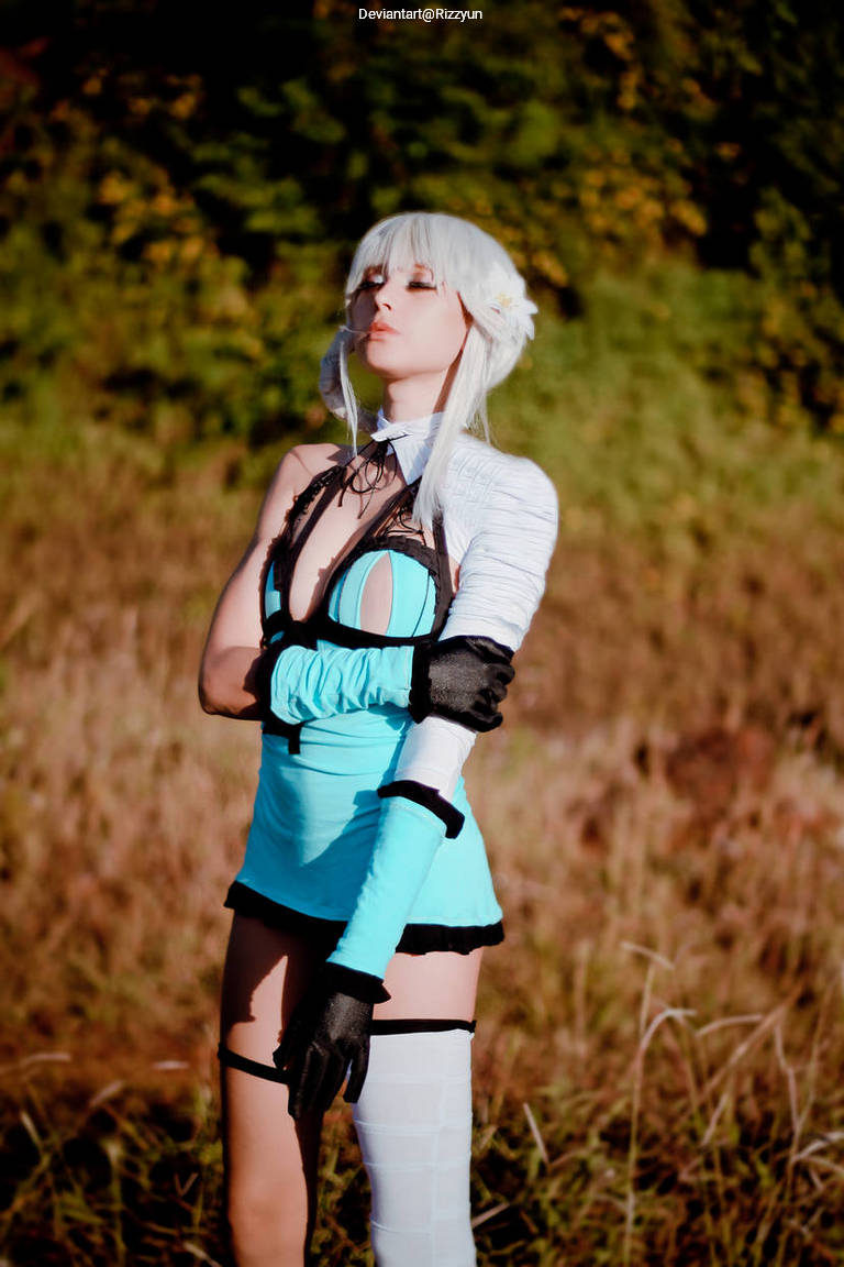 A character in a turquoise outfit with black trim, featuring long sleeves and gloves, posing confidently in a grassy area with a blurred natural background.