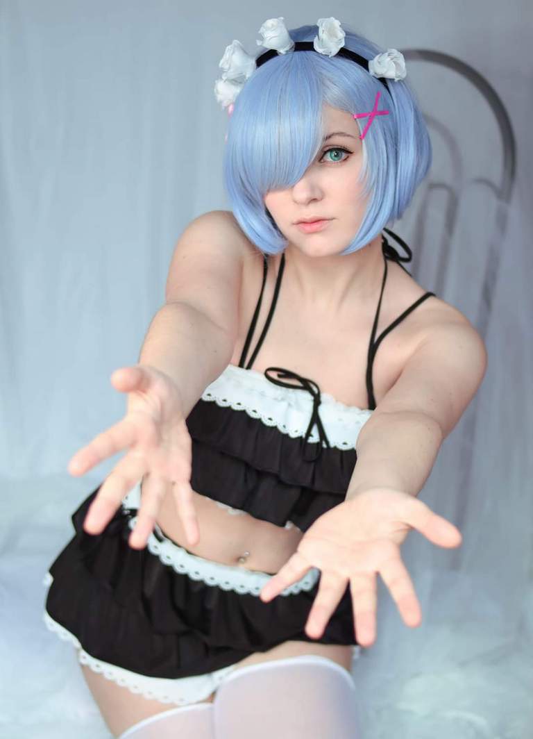 Person in a blue wig with flowers, wearing a black and white frilly outfit, extending their hands forward.