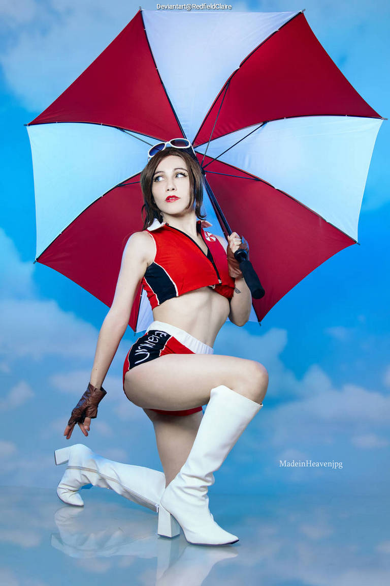 A person in a red and white outfit poses with an umbrella, wearing sunglasses and white boots against a blue sky background.
