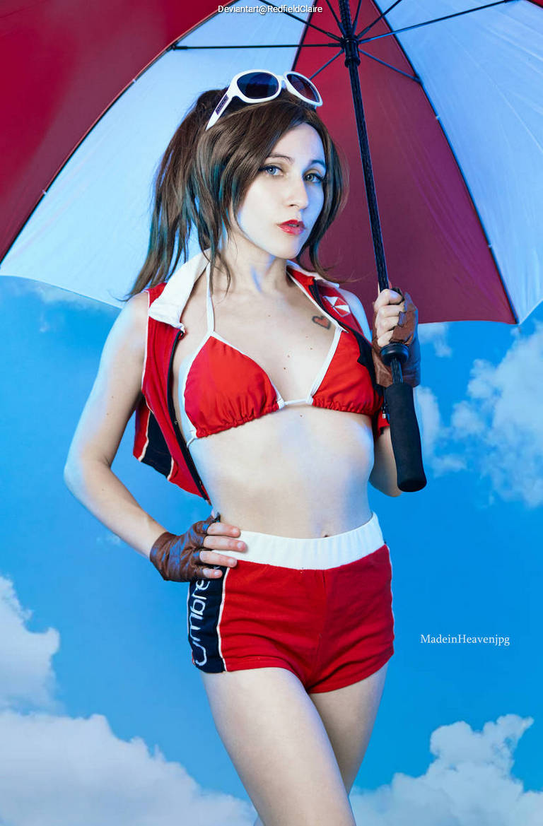 A person in a red and white bikini-style outfit holds a large umbrella while standing against a blue sky with clouds.