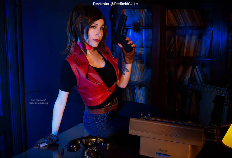 A woman with shoulder-length dark hair poses confidently at a desk, holding a handgun. She wears a red vest, black top, and gloves, with a vintage typewriter and telephone visible beside her. The background features dark blue lighting and bookshelves.