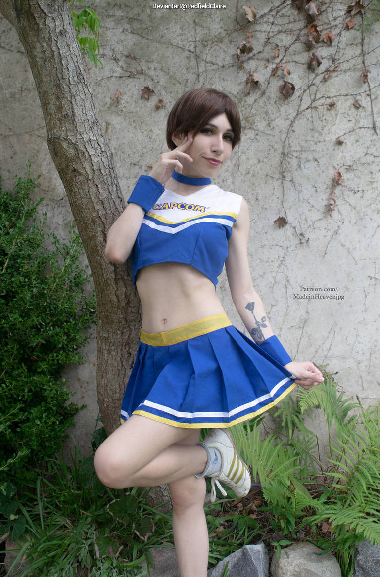A person in a blue and white cheerleader outfit posing playfully in front of a tree and greenery.