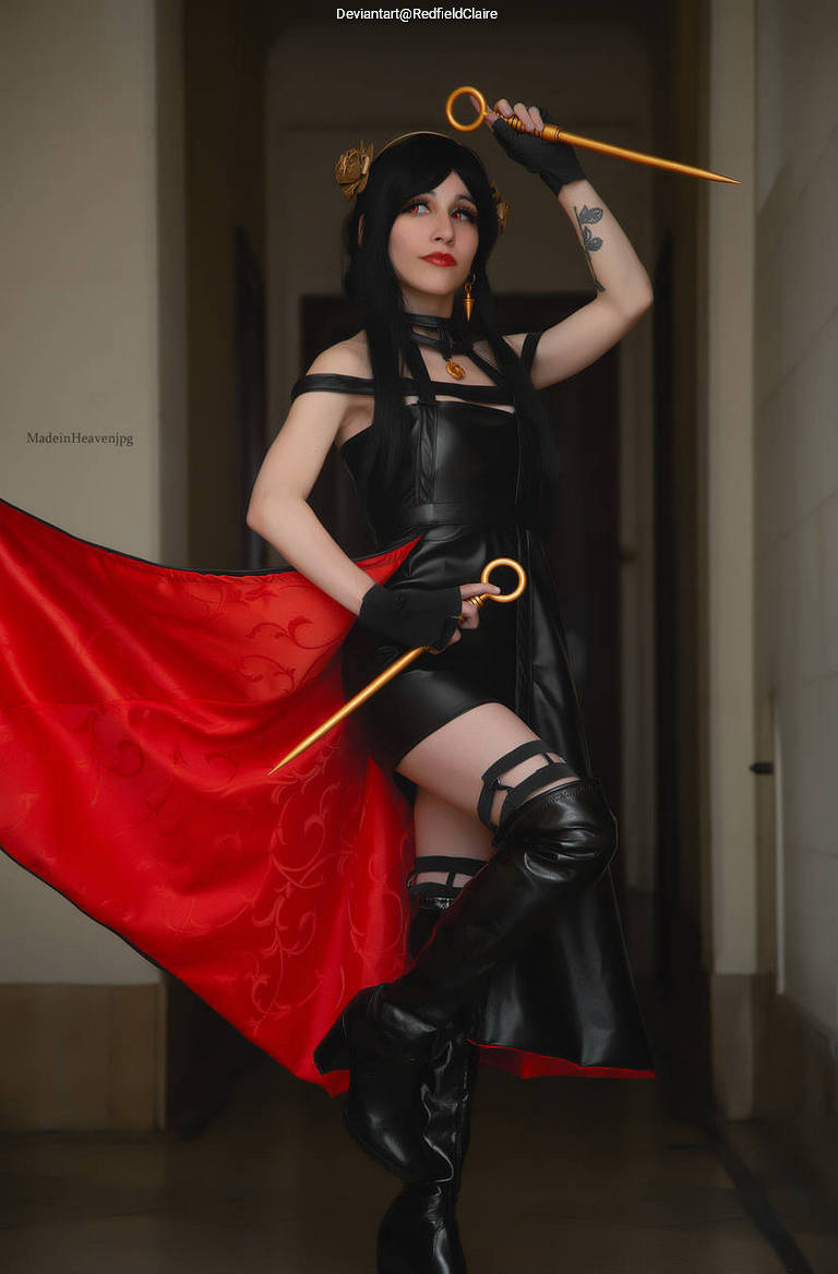A person dressed in a black and red cosplay outfit, holding a golden weapon, striking a dramatic pose indoors.
