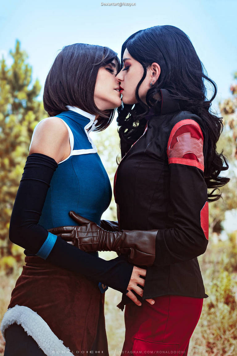 Two women cosplaying as characters, leaning in for a kiss against a natural outdoor backdrop.