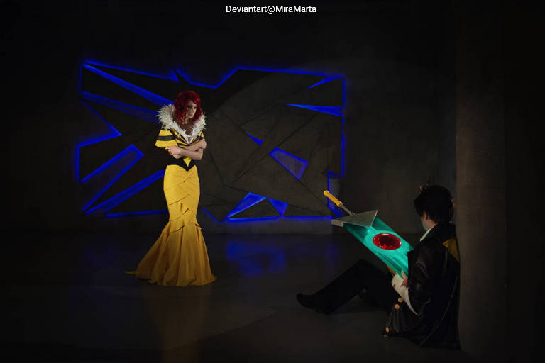 A woman in a yellow gown with white feather accents stands confidently, while a man in dark attire sits nearby, holding a colorful sword with a red emblem.