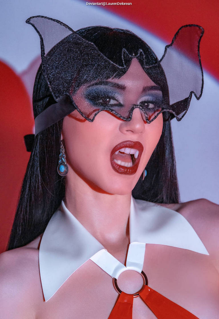 A person with dark hair and dramatic makeup wearing a bat-themed headpiece and a stylish outfit, striking a fierce pose.