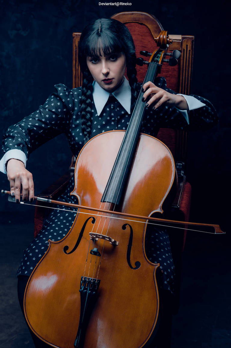 A young woman with dark hair styled in braids is sitting on a vintage chair, playing a cello. She wears a black dress with white polka dots and looks intently at the instrument.