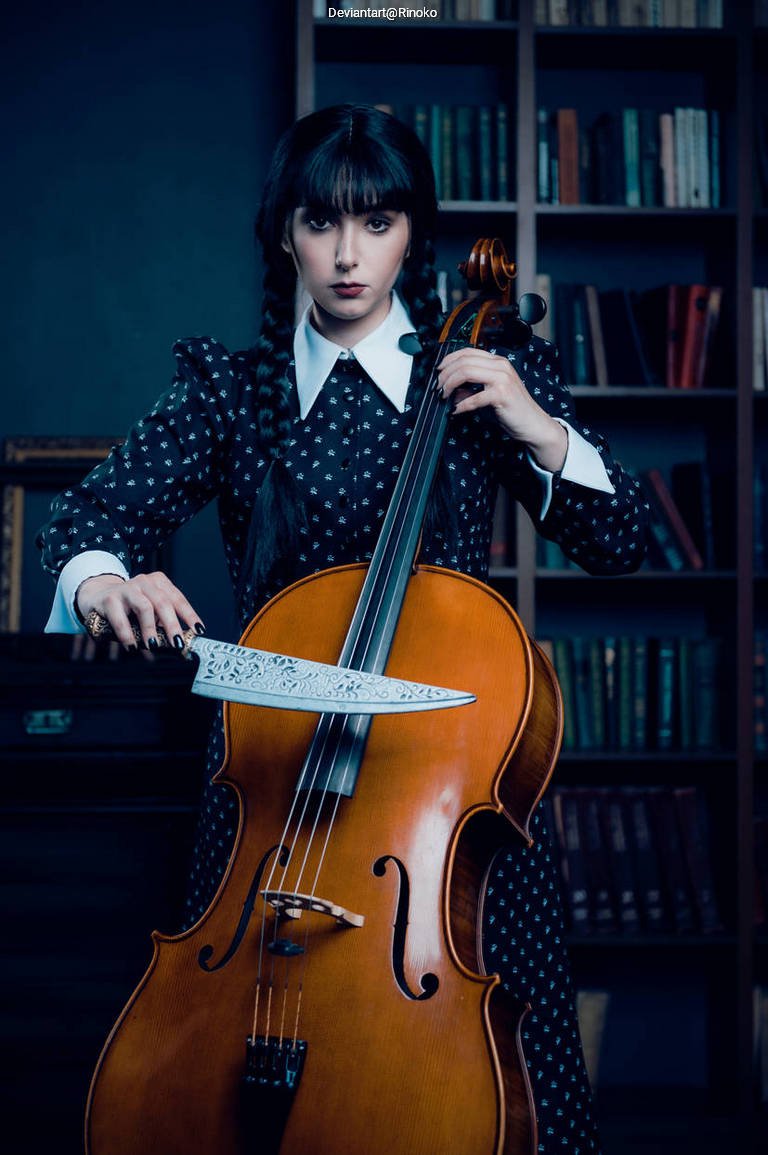 A person in a dark polka-dotted dress poses with a cello in one hand and a large ornate knife in the other, set against a backdrop of bookshelves filled with books.