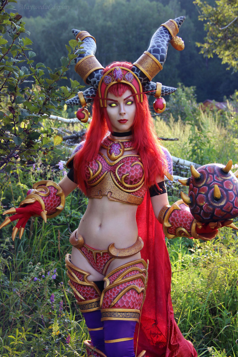 A cosplayer dressed as a fantasy character, featuring elaborate armor, horns on the head, and holding a spiked ball, set in a lush green outdoor environment.