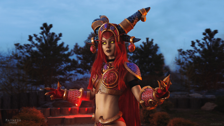 A woman in an elaborate fantasy costume with red hair, intricate armor, and glowing eyes, posing outdoors against a twilight background.