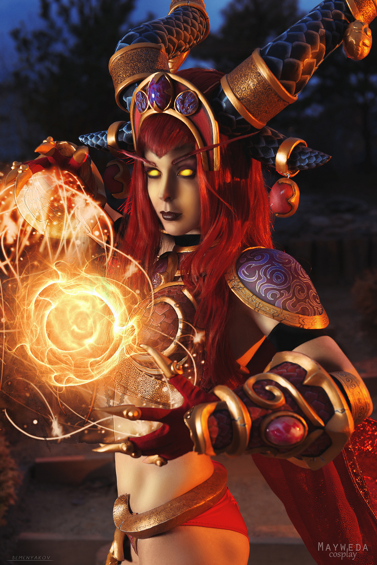 A character in elaborate fantasy cosplay with red hair and yellow eyes, holding a glowing orb of magic.