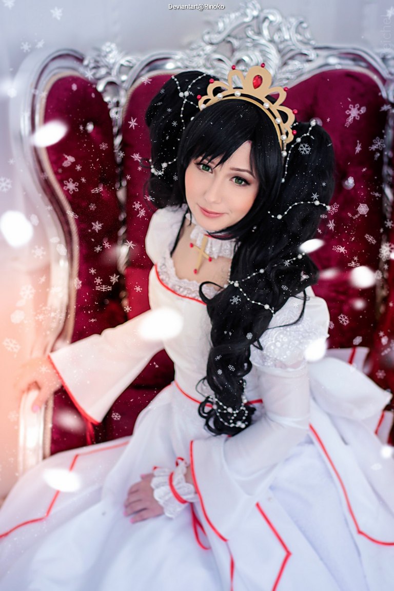 A female cosplayer in a regal white dress with red accents, sitting on a plush throne. She has long black hair adorned with large pigtails and a golden crown, surrounded by a snowy background.