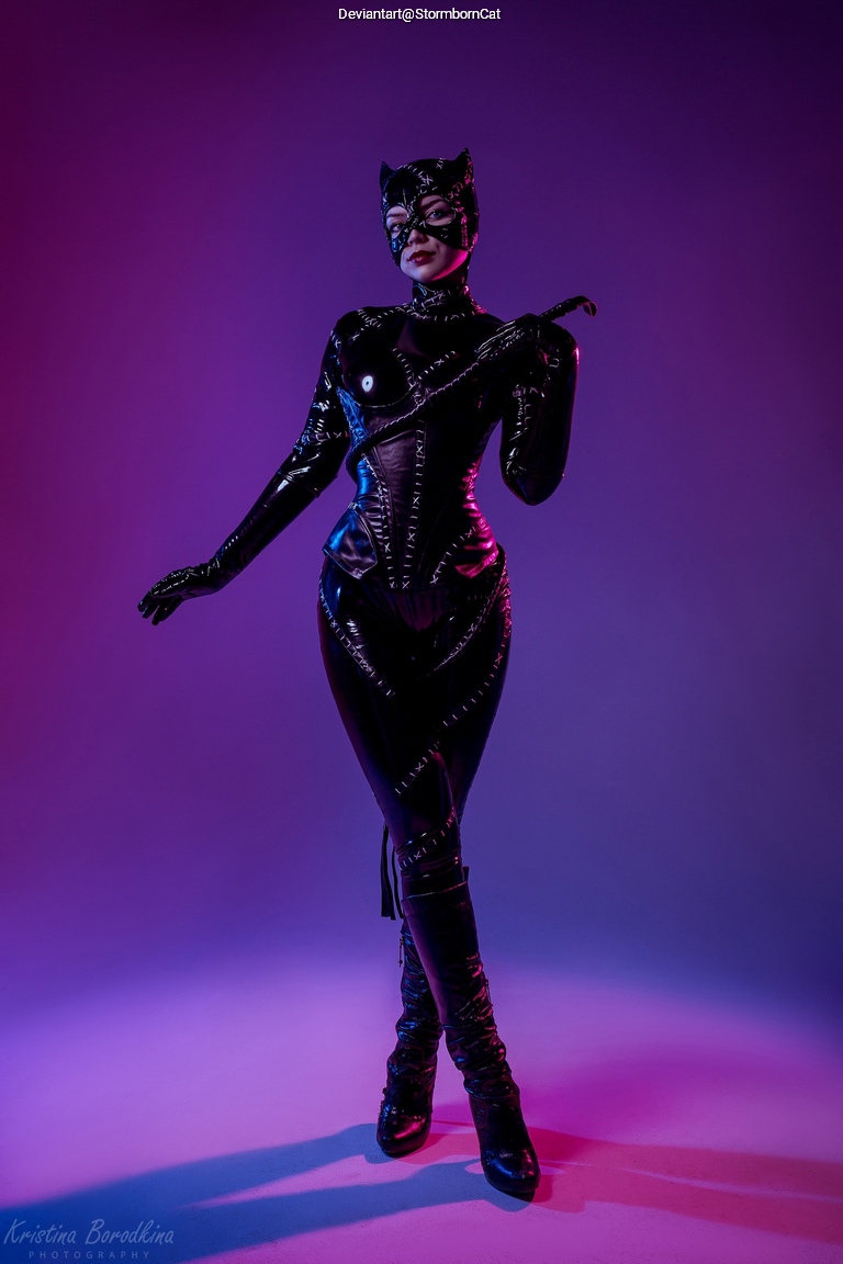 A model poses in a sleek black catsuit and cat mask, set against a purple gradient background, exuding confidence and allure.