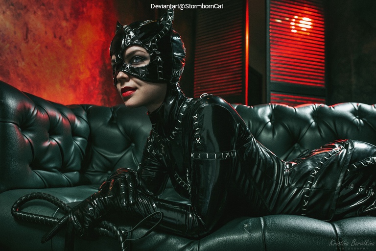 A woman in a black cat costume lounges on a dark green leather couch, with a seductive pose and a cat-like mask. The background features a red ambient light, enhancing the dramatic atmosphere.