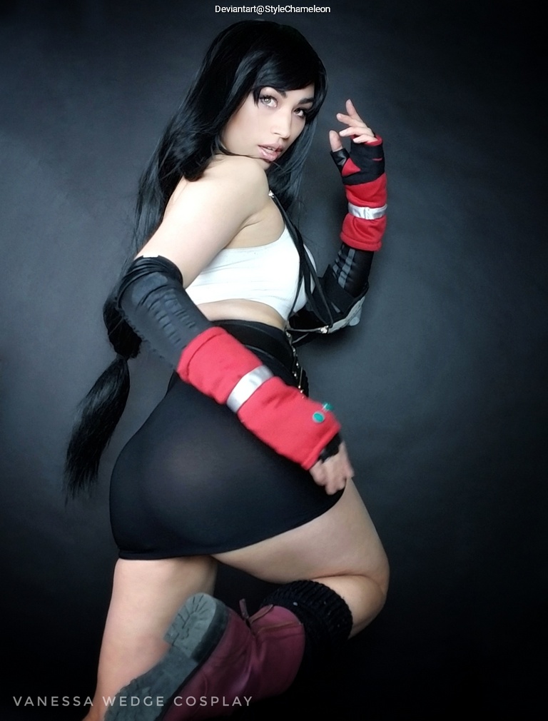 A person posing in a costume resembling a character, with long black hair, wearing a crop top and skirt, highlighted against a dark background.