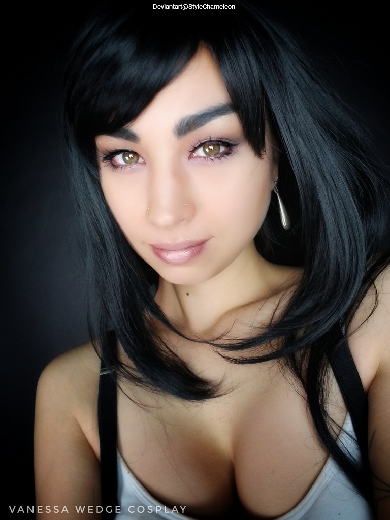 Close-up portrait of a person with long black hair, wearing makeup and a sleeveless top. The background is dark, highlighting the subject's features.