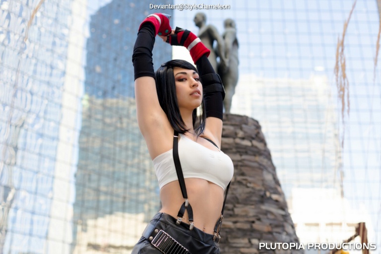 Young woman in a cropped white top and black pants, striking a pose outdoors with a modern building in the background.