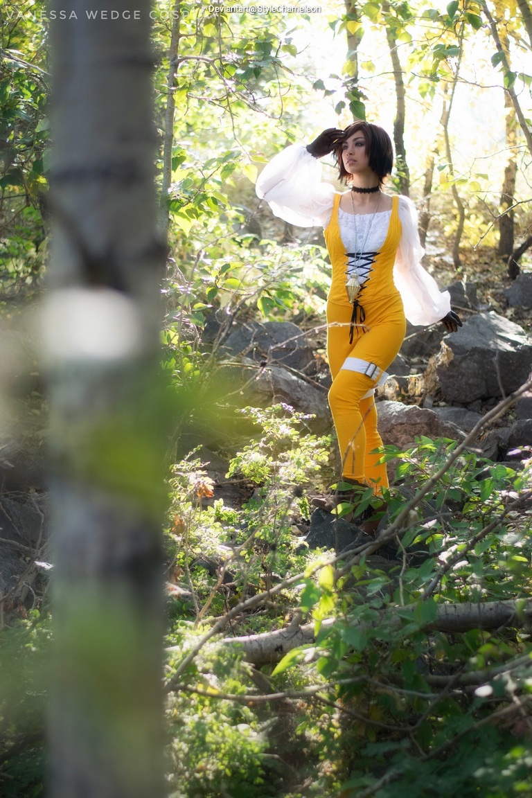 A person in a bright yellow outfit stands among green foliage, striking a pose while looking off to the side. The scene is illuminated by soft natural light, creating a serene atmosphere.