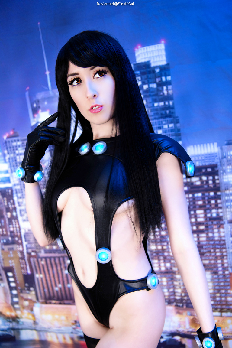 Cosplay of a character wearing a glossy black bodysuit with blue accents, posing in front of a cityscape background.