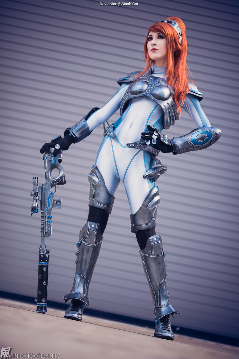 A person in a futuristic silver and blue armored costume posing with a weapon in a modern setting.