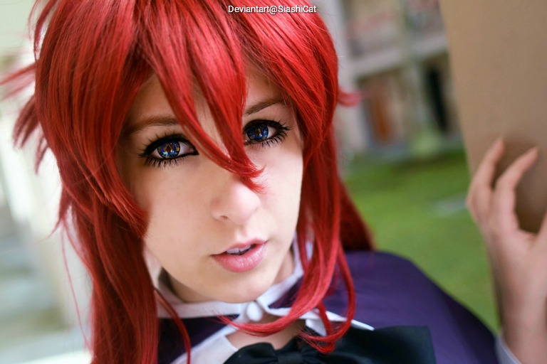Close-up portrait of a person with striking red hair and large, expressive blue eyes, wearing a purple cape and a white collar.