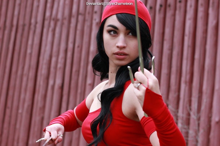 A woman in a red outfit striking a dynamic pose, holding a weapon, with a focused expression against a wooden background.