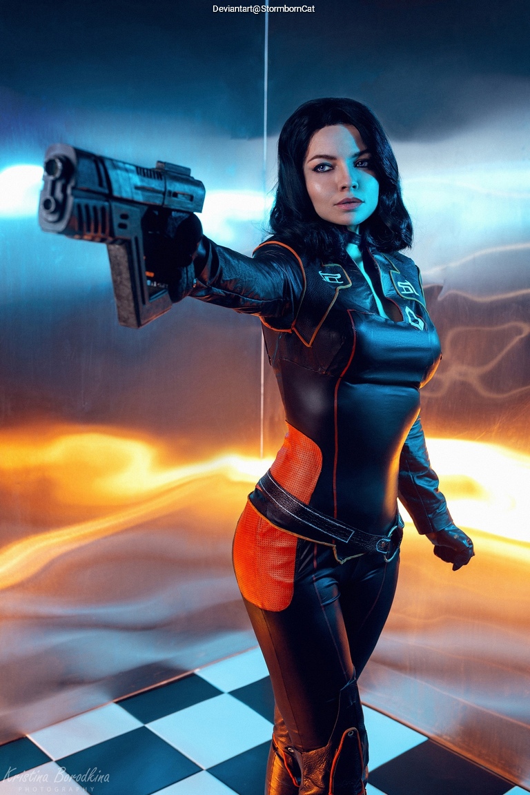 A woman in a futuristic black and orange bodysuit is aiming a gun, with an intense expression, against a colorful background of blue and orange lighting.