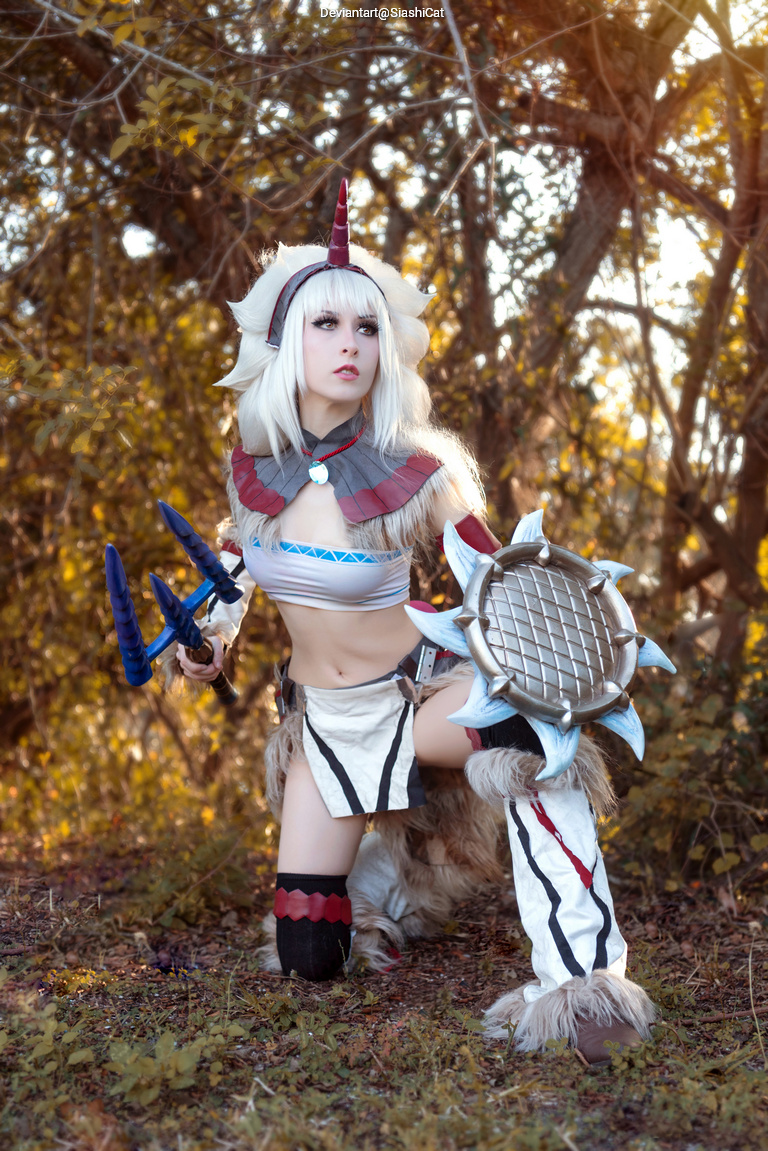 A character in a detailed costume with a horned headpiece, wielding a shield and spear, poses in a natural outdoor setting surrounded by foliage.