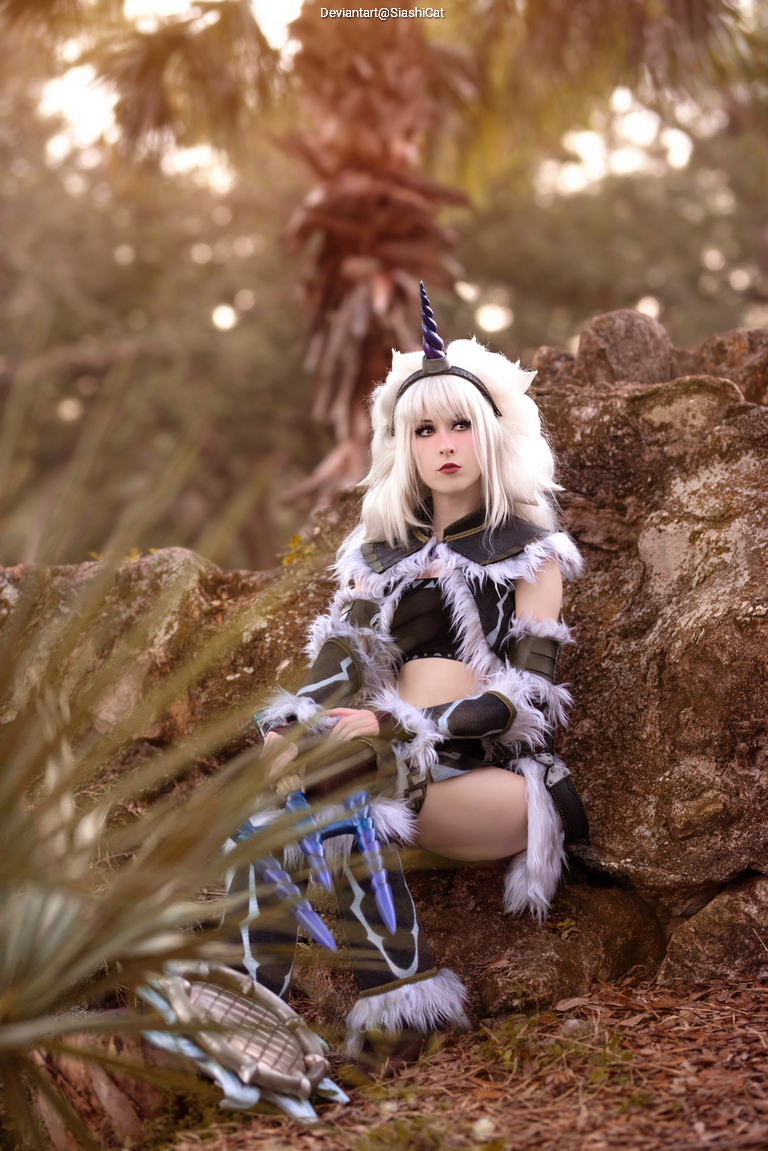 A person dressed in a fantasy-themed costume with animal features, including a unicorn horn and fur accents, sitting on a rock amidst greenery and soft natural lighting.