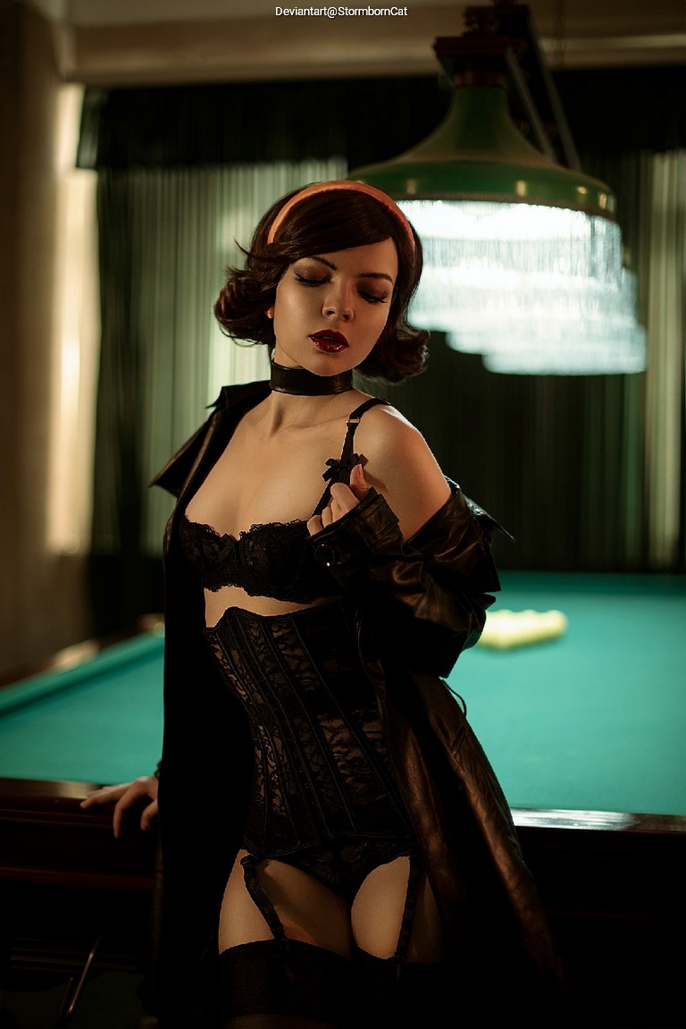 A woman in a black corset and stockings poses confidently in front of a pool table, wearing a long leather coat and a choker, with softly styled hair and a sultry expression.