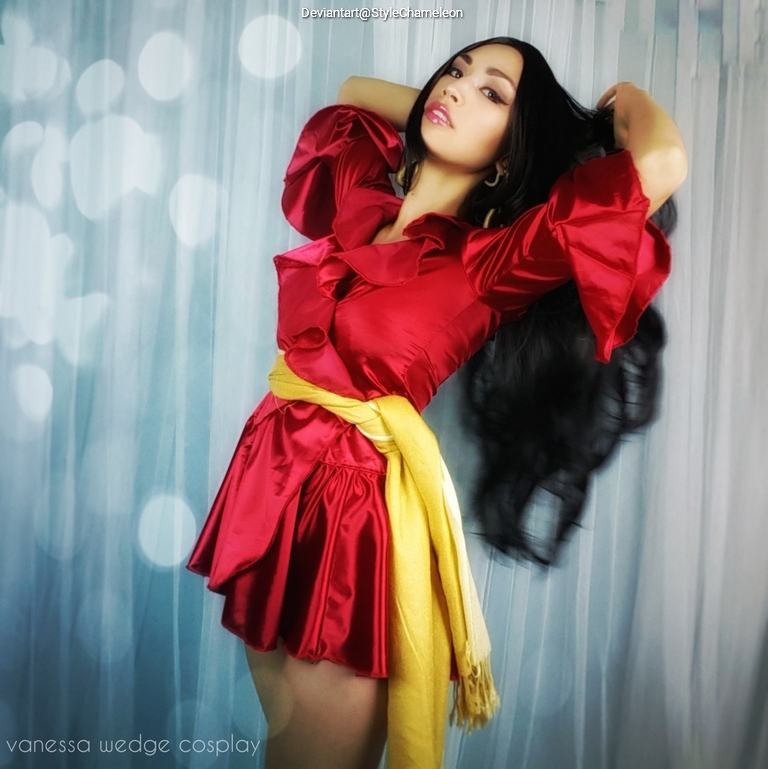 A person in a red satin dress with puffed sleeves, posing with long dark hair while holding their hair back. They also wear a yellow sash, and the background features light bokeh effects.