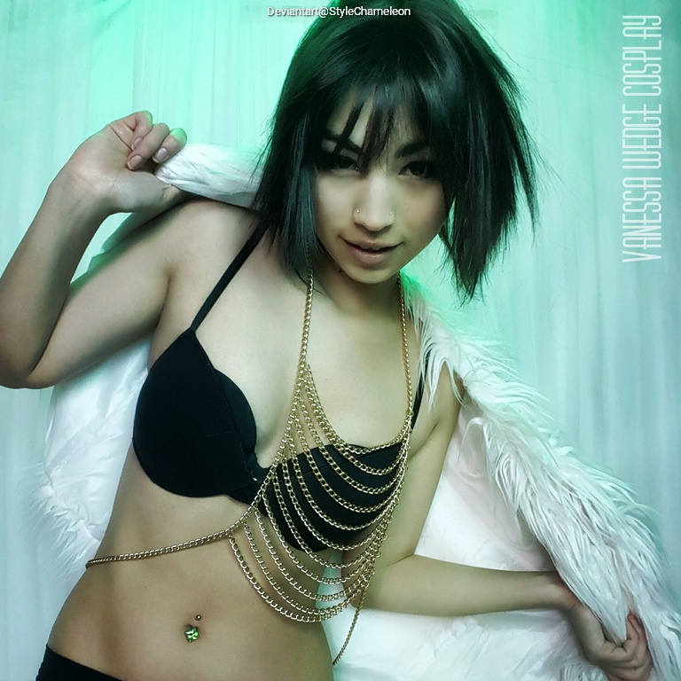 A confident model wearing a black bra and a chain necklace, partially draped in a white fur coat, posing against a green-lit background.