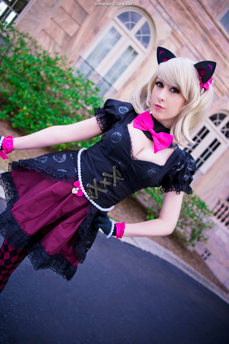 A person in a stylish cosplay outfit featuring black and pink colors, with cat ears and a bow tie, striking a pose outdoors.