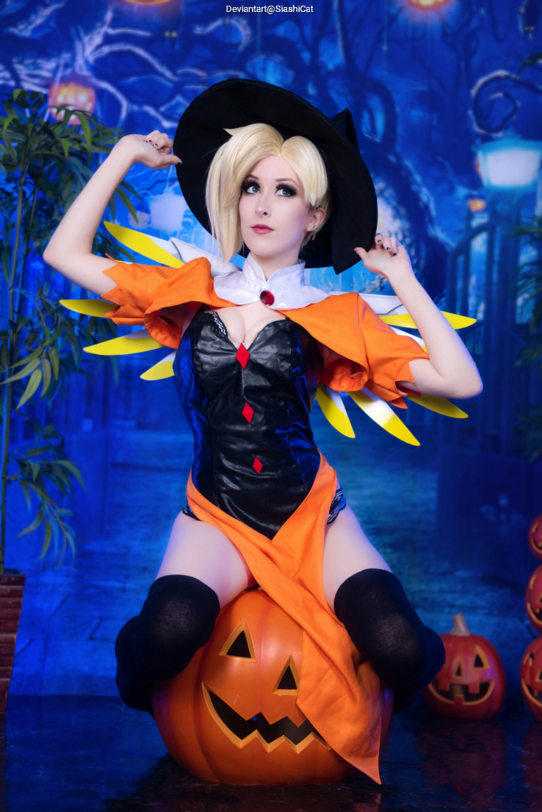 A person in a whimsical Halloween costume with a witch hat and colorful cape sits playfully on a large pumpkin, set against a dark and atmospheric backdrop.